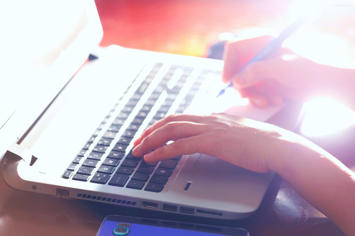 Hands typing on a laptop keyboard with a bright light in the background