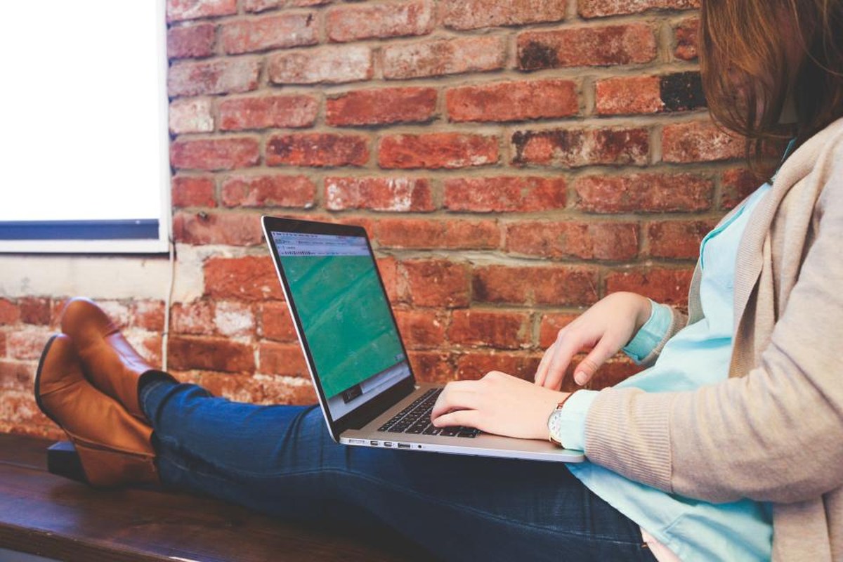 A person working on an app interface at a laptop near a brick wall