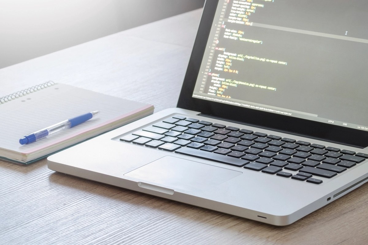 A laptop open with code visible on the screen, beside a notebook